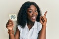 Beautiful african young woman holding paper with aquarius zodiac sign smiling with an idea or question pointing finger with happy