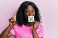 Beautiful african young woman holding paper with cross symbol surprised with an idea or question pointing finger with happy face,
