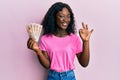 Beautiful african young woman holding 10 united kingdom pounds banknotes doing ok sign with fingers, smiling friendly gesturing