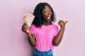 Beautiful african young woman holding 10 united kingdom pounds banknotes pointing thumb up to the side smiling happy with open