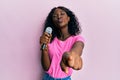 Beautiful african young woman singing song using microphone pointing to camera looking at the camera blowing a kiss being lovely Royalty Free Stock Photo