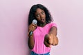 Beautiful african young woman singing song using microphone pointing to camera in shock face, looking skeptical and sarcastic, Royalty Free Stock Photo