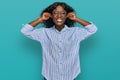 Beautiful african young woman wearing casual clothes and glasses smiling pulling ears with fingers, funny gesture Royalty Free Stock Photo