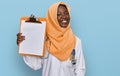 Beautiful african young woman wearing doctor stethoscope holding clipboard looking positive and happy standing and smiling with a Royalty Free Stock Photo