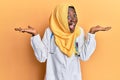 Beautiful african young woman wearing doctor uniform and hijab celebrating crazy and amazed for success with arms raised and open Royalty Free Stock Photo