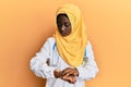 Beautiful african young woman wearing doctor uniform and hijab checking the time on wrist watch, relaxed and confident Royalty Free Stock Photo