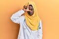 Beautiful african young woman wearing doctor uniform and hijab making fun of people with fingers on forehead doing loser gesture Royalty Free Stock Photo