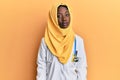 Beautiful african young woman wearing doctor uniform and hijab relaxed with serious expression on face Royalty Free Stock Photo