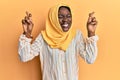 Beautiful african young woman wearing traditional islamic hijab scarf gesturing finger crossed smiling with hope and eyes closed Royalty Free Stock Photo