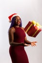Beautiful Afro American girl in a dress and Santa hat is catching falling presents, looking at camera and smiling, isolated on Royalty Free Stock Photo