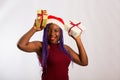 Beautiful Afro American girl in a dress and Santa hat is danci falling presents, looking at camera and smiling, isolated on white Royalty Free Stock Photo