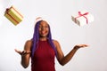 Beautiful Afro American girl in a dress and Santa hat is catching falling presents, looking at camera and smiling, isolated on Royalty Free Stock Photo