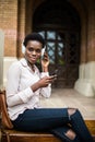 Beautiful afro american girl listening to music through headphones sitting on a bench. female with afro hair watching video on sma