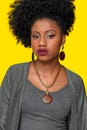 beautiful afro teenager girl wearing wooden necklace and earrings with gold details, wearing gray clothes isolated on yellow back Royalty Free Stock Photo