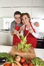 Beautiful American couple working at home kitchen in apron mixing vegetable salad smiling happy Royalty Free Stock Photo