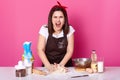 Beautiful angry cook kneads dough and screams loud, being sick and tired of preparing homemade pastry. Furious brunette woman