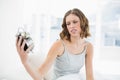 Beautiful annoyed woman holding an alarm clock looking at it sitting on her bed