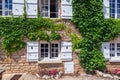 Beautiful antique old brick house rustic window with white wooden shutters, flowers, entwined green ivy covered exterior wall Royalty Free Stock Photo