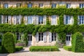 Beautiful antique old brick house rustic window with white wooden shutters, flowers, entwined green ivy covered exterior Royalty Free Stock Photo