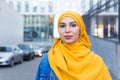 Beautiful Arabic muslim woman wearing yellow hijab, stylish female face portrait over city street. Royalty Free Stock Photo