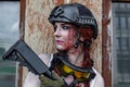 Beautiful army girl with a bloody face with rifle in camouflage clothes in urban scene, getting rest. portrait, close up