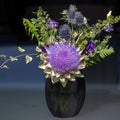 Purple artichoke flower with thistles in a small black glass vase against dark background. Royalty Free Stock Photo