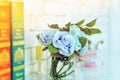 Beautiful artificial blue roses in glass vase on a white table with blured image of three books