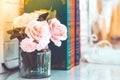 Beautiful artificial pink roses in glass vase on a white table with blured image of three books Royalty Free Stock Photo