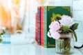 Beautiful artificial pink roses in glass vase on a white table with blured image of three books