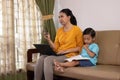 A beautiful Asian business mother uses a cellphone and laptop while teaching her son