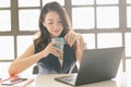 Beautiful Asian business woman holding coffee cup in hands enjoy smell while using laptop computer sits work at home office. Royalty Free Stock Photo