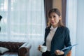 Beautiful asian business woman holding a cup of coffee and documents while looking at the camera in her office Royalty Free Stock Photo