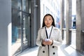 Beautiful asian business woman looking at camera and smiling, holding phone in hands, near office center outside Royalty Free Stock Photo