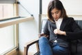 A beautiful asian business woman sitting on sofa holding smart phone and checking her suit for meeting today. Royalty Free Stock Photo