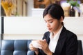 A beautiful asian business woman sitting on sofa and looking cup of hot coffee in her hand. Royalty Free Stock Photo