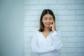 Beautiful asian business woman is standing against a white brick wall with her hands on her cheeks smiling and closing her eyes. Royalty Free Stock Photo