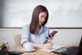 Beautiful asian business woman working sitting at her desk in the office and texting on the phone and working on laptop Royalty Free Stock Photo