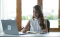 Beautiful Asian businesswoman analyzes charts using laptop calculator at the office.