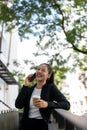 Beautiful Asian businesswoman is enjoying talking on the phone while taking a coffee break outdoors Royalty Free Stock Photo