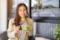 Beautiful Asian businesswoman having brunch, holding a salad bowl at the cafe Royalty Free Stock Photo