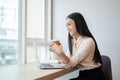 Beautiful Asian businesswoman is having a morning coffee while working on her laptop in the office Royalty Free Stock Photo