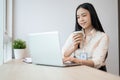 Beautiful Asian businesswoman is having a morning coffee while working on her laptop in the office Royalty Free Stock Photo