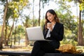 A beautiful Asian businesswoman is sitting on a bench in a city park, and working on her laptop Royalty Free Stock Photo