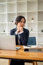 A beautiful Asian businesswoman sits at her desk, looking aside with a thoughtful face Royalty Free Stock Photo