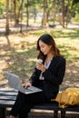 A beautiful Asian businesswoman is sitting on a bench in a city park, and working on her laptop Royalty Free Stock Photo