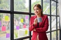 A beautiful Asian businesswoman stands by the window with a cup of coffee in her hand Royalty Free Stock Photo