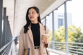 A beautiful Asian businesswoman is walking along a skywalk in the city with her takeaway coffee cup Royalty Free Stock Photo