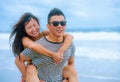 beautiful Asian Chinese couple with boyfriend carrying woman on her back and shoulders at the beach smiling happy in love