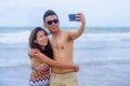 beautiful Asian Chinese couple taking selfie photo with mobile phone camera smiling joyful having fun on the beach Royalty Free Stock Photo