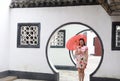 Beautiful Asian Chinese woman in traditional chi-pao cheongsam hold red parasol in a garden stand under arched door Royalty Free Stock Photo